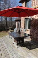 Full set on wooden deck: table, red umbrella, four chairs.