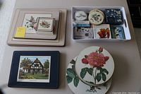 Assorted placemats and coasters laid out on a table, showing various floral and architectural images on rectangular and round pieces.
