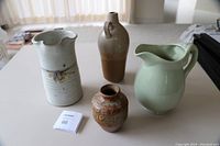 Four pottery pieces shown on a table, three jugs and one vase in different sizes and finishes
