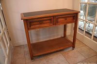 Full view of the hardwood hall table showing two drawers and lower cane shelf on wheels.