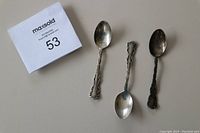 Three Birks sterling silver coffee spoons arranged side by side with auction tag. One spoon is very tarnished, others moderately tarnished.