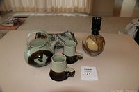 Photo of ceramic teapot and two mugs with brown and cream glaze, and a La-Tee-Da lamp with a marbled brown and tan ceramic base and black lamp socket on a table
