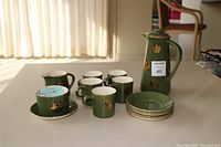 Full view of green coffee set on table with coffee pot, sugar dish, creamer, 5 mugs and 6 saucers