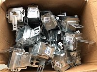 Box filled with approximately 20 metal electrical boxes showing metallic surfaces and mounting brackets, packed loosely in a cardboard box.