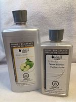 Two bottles of Lampe Berger home fragrance refill. Larger bottle labeled Green Apple, smaller bottle labeled So Neutral.