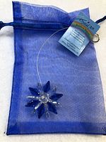 Photo of the new Crystal Art suncatcher showing a blue and clear crystal star/flower shape, hanging loop wire, blue organza pouch, and product tag.