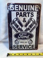 Photo of rectangular tin sign featuring the text 'GENUINE PARTS & Ford SERVICE SINCE 1903' with piston graphics.