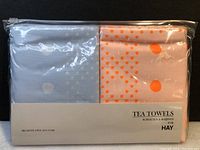 Photo of two tea towels in original clear plastic packaging, showing light blue and off-white towels with dot patterns and label with brand and size.