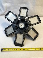 Front view of LED light with six foldable panels laid flat with a measuring tape showing about 10 inches in diameter.