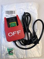 Overall view of new safety emergency stop switch with red cover and attached power cord, on white padded envelope packaging.