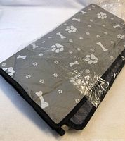 Gray pet protector folded, showing paw and bone print side, wrapped in plastic.