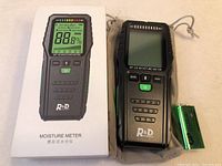 Photo showing the moisture meter next to its original branded white box and a 9V battery connected by a wire.