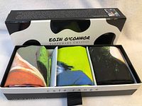 Photo of the box containing 3 folded tea towels with colorful cow designs by Eoin O'Connor.