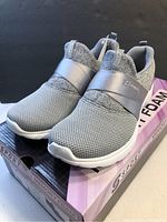 Side angle of new grey Skechers sport shoe on box showing mesh upper and elastic strap.