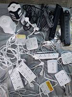 Photo showing multiple power surge protector bars and cubes with various outlets and USB ports on a fabric surface.