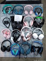 Full lot of 17 headsets in various colors laid out for display, showing wide assortment including wired and wireless models with visible cables and accessories.