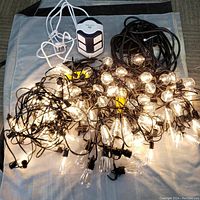 Photo showing three string lights with clear incandescent bulb covers, two black triple plug cables, and one white multifunctional power tower power strip.