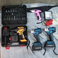 Overview of all items showing cordless drills, screwdriver, drill bits in case, batteries, and LED work light