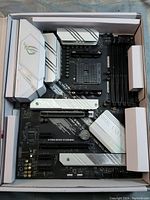 Top view of Asus STRIX ROG B550-A Gaming motherboard in original packaging showing black PCB, white and silver heatsinks, PCIe slots and memory slots.