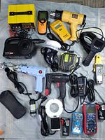 Full view of all tools spread out on cloth with battery charger, pump, heat gun, stud finders, endoscope, stapler and multimeters visible
