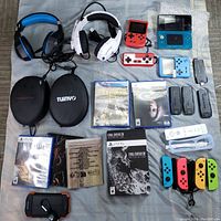 Multiple handheld gaming consoles (red retro unit, red GameBoy style, turquoise 3DS, silver DS Lite, blue Game Boy Micro) and four grey battery modules