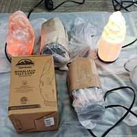 Five Himalayan salt lamps shown; four orange lamps, two lit, and partially packaged; one white carved lamp lit.