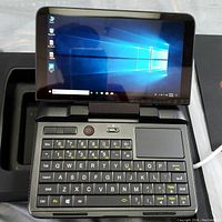 Handheld PC open in tray showing screen, keyboard and touchpad