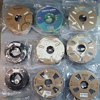 Top view of all 9 rolls of 3D printer filament on a flat surface, showing various brand labels and cardboard spools.