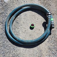 Coiled blue flexible suction hose laid out on gravel surface showing full hose length and tubing material.
