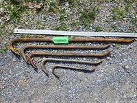 Five rusted crow bars laid out on gravel with measuring stick showing size, items range from small to large with visible rust and wear.
