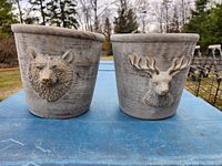 Pair of rustic animal figure flower pots on a blue surface outdoors, showing bear and moose head designs
