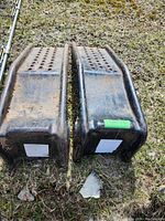 Pair of steel automotive ramps with surface holes, visible rust and dirt, placed on grass outdoors.