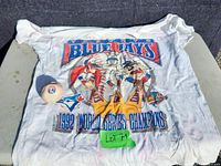 White 1992 Toronto Blue Jays World Series Champions T-shirt displayed with Montreal Expos hacky sack on concrete surface showing condition of items