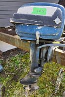 Side view of vintage Evinrude outboard motor showing blue and white paint with wear and propeller.