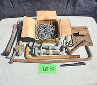 Top view of assorted gate and fencing hardware showing box of bar wires, bolts, hooks, metal rods, metal plate with hook and spring. Items show rust and wear.