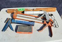 All items in the lot including caulking guns, wooden level, and sanding block on a white surface.