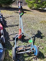 Wide view of the reel mower and electric trimmer placed on grass outside