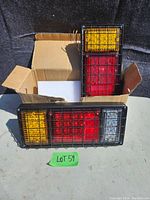 Pair of new LED tail lights with amber, red, and clear lens sections, wired and protected by black metal grids, displayed with original box and foam insert.