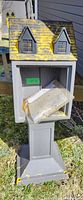 Full view of the outdoor sharing library or pantry box shaped like a house, showing yellow paint splatters and wear.