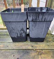 Front view of two large black plastic planters outdoors showing water staining and overall condition.