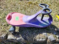 Side view of Plasma Car ride-on toy showing purple and pink plastic body and black steering wheel shaped with two grips.