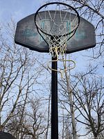 Photo of black basketball backboard, orange hoop, white net against sky background