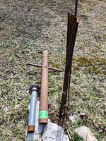 Two metal post pounders on grass, one large with T-handle and significant rust, other smaller with gray steel and threaded end.
