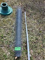 Roll of rolled galvanized chicken wire next to a tape measure on grass, showing an approximate length of 2 meters.