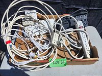 Photo of assorted power bars, plug-in blocks, and cords in a cardboard box; items are tangled together.