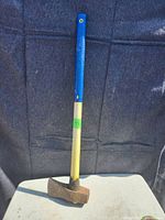 Image showing the full maul with rusted head and blue/yellow handle against a dark fabric background.