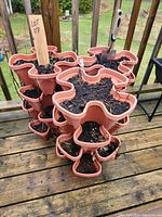Stacked view of terracotta-colored four-lobed plastic planters filled with soil on a wooden deck.