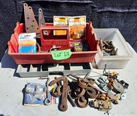 Wide shot showing full lot with red tray caddy holding hardware items and additional plastic container with metal parts. Includes pulleys, hooks, hinges, castors, and small parts.