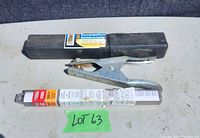 Photo showing black plastic case with label for E7018 welding electrodes and a silver metal replacement ground clamp.