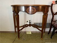 Front view of demilune table showing apron inlay and tapered legs joined by metal stretcher